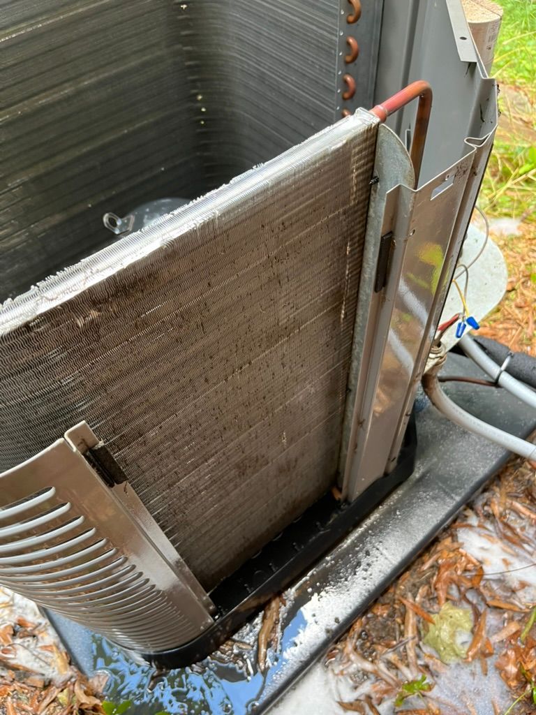 Damaged outdoor HVAC condenser coil with bent fins and rusted frame beside a wall and leaves