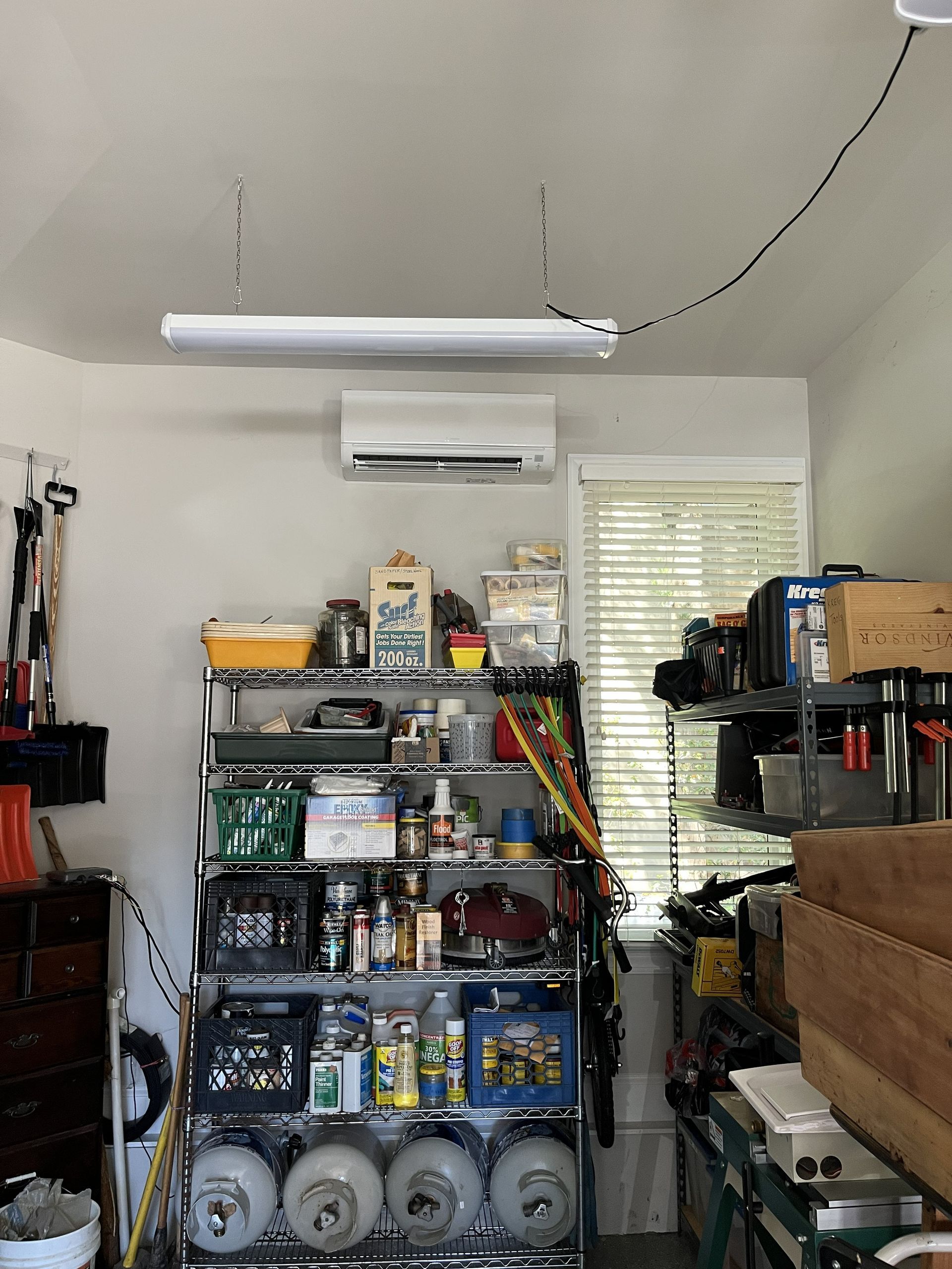 Garage storage area with metal shelves, tools, boxes, and stacked tires under a fluorescent light.