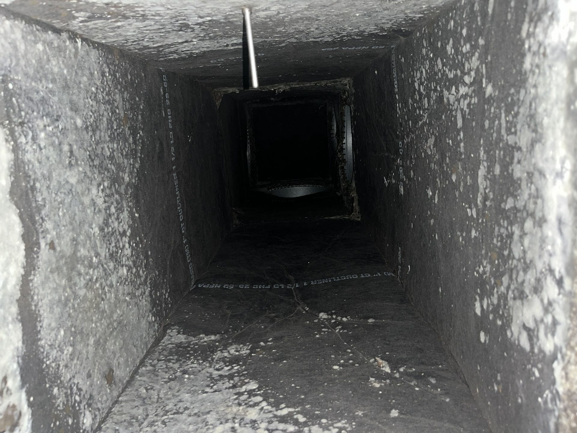Dark, narrow square ventilation duct with a small opening at the far end
