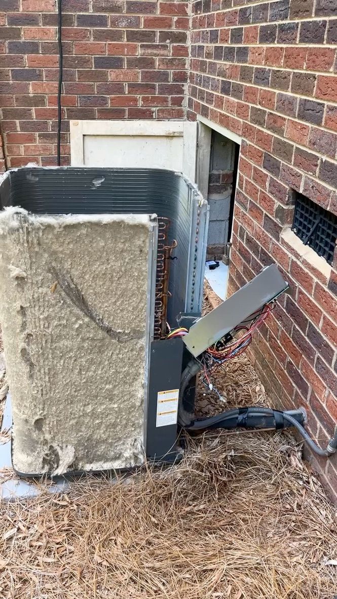 Damaged outdoor HVAC unit beside a brick house wall, with a bent panel and exposed parts