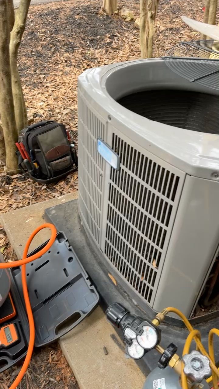 Outdoor HVAC service scene with a gray condenser unit, gauges, and tools on the ground