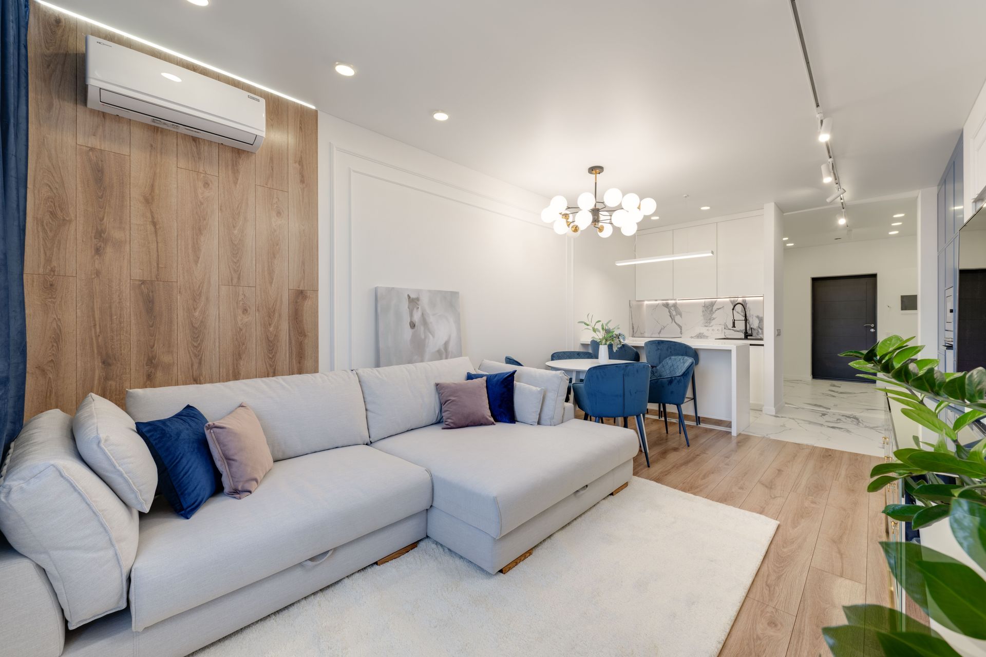 Bright modern living room with gray sectional, blue chairs, wood accent wall, and kitchen area in back