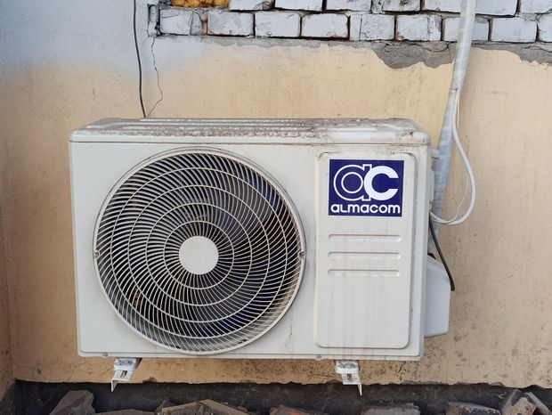 Outdoor air conditioner unit on a beige wall with a circular fan and C C logo.