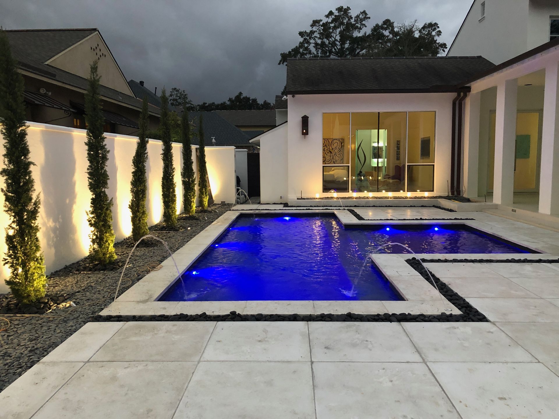 Modern backyard patio with lit swimming pool and blue underwater lights at dusk