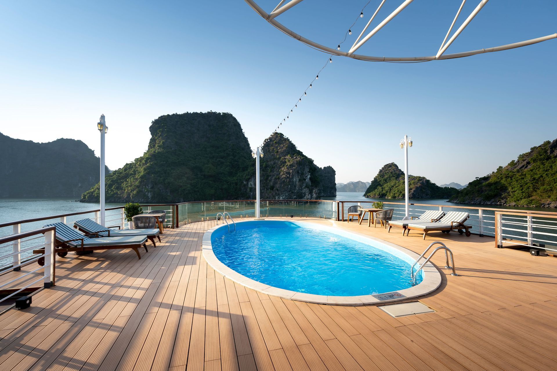 Wooden deck with a blue plunge pool overlooking calm water and green islands under a clear sky