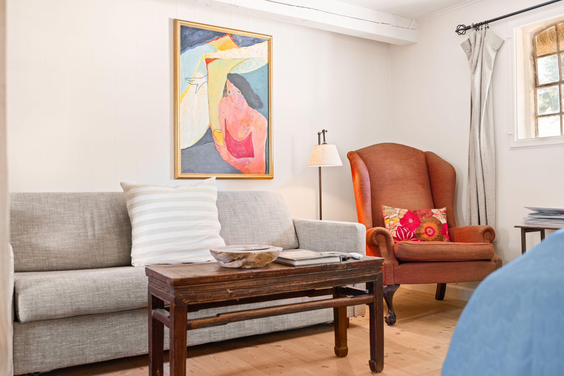A living room with a couch , chair , coffee table and painting on the wall.