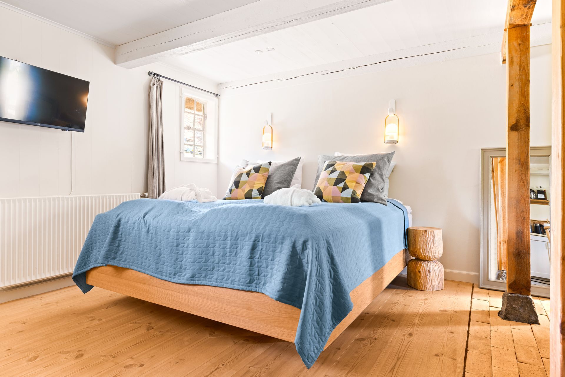 A bedroom with a bed , mirror and wooden beams.
