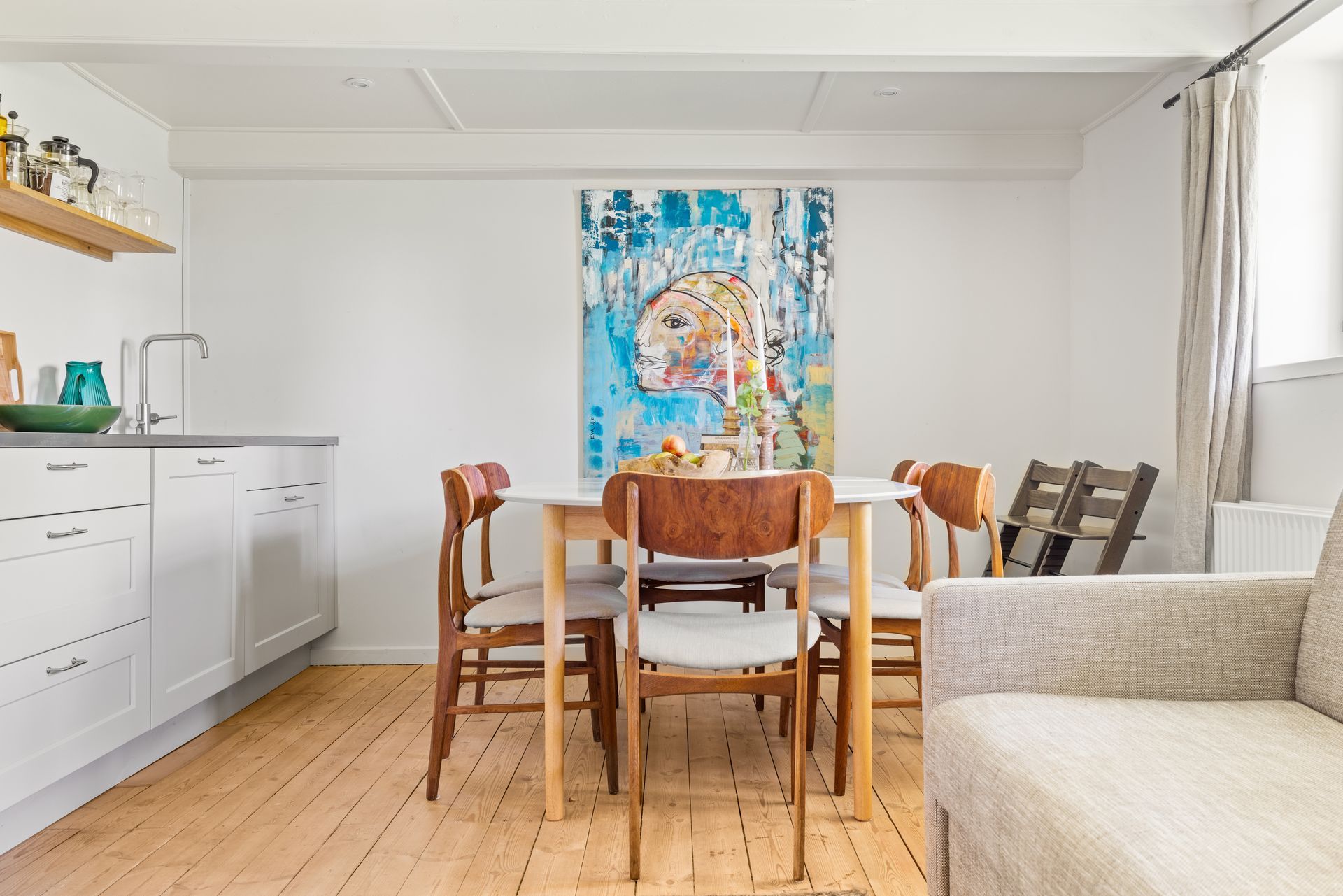 A dining room with a table and chairs and a painting on the wall.