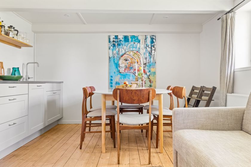 A dining room with a table and chairs and a painting on the wall.