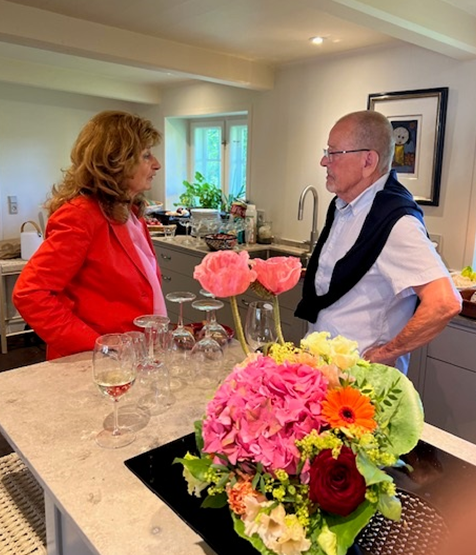 A man and a woman are standing next to a table with flowers and wine glasses.