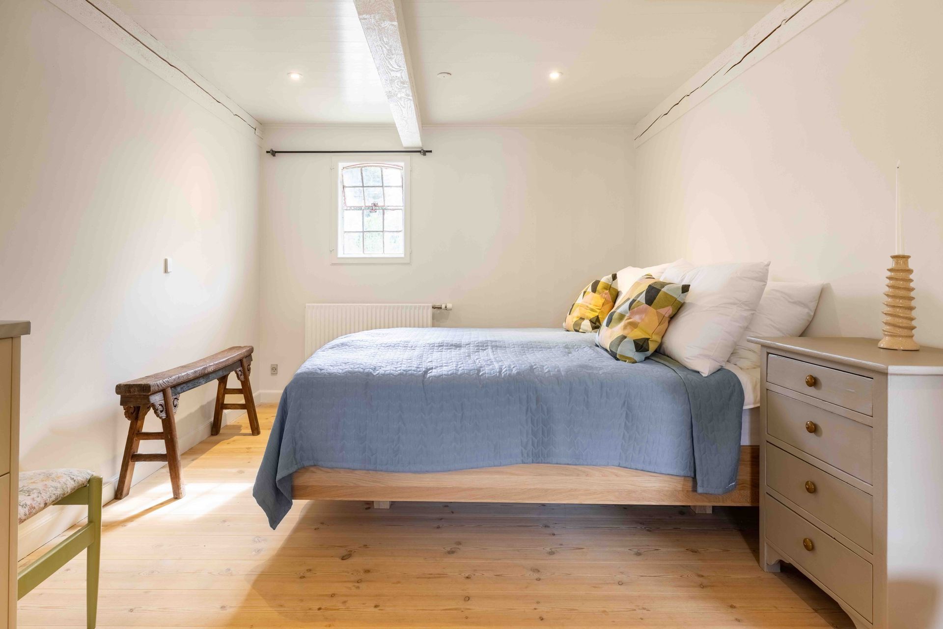 A bedroom with a bed , dresser , bench and window.