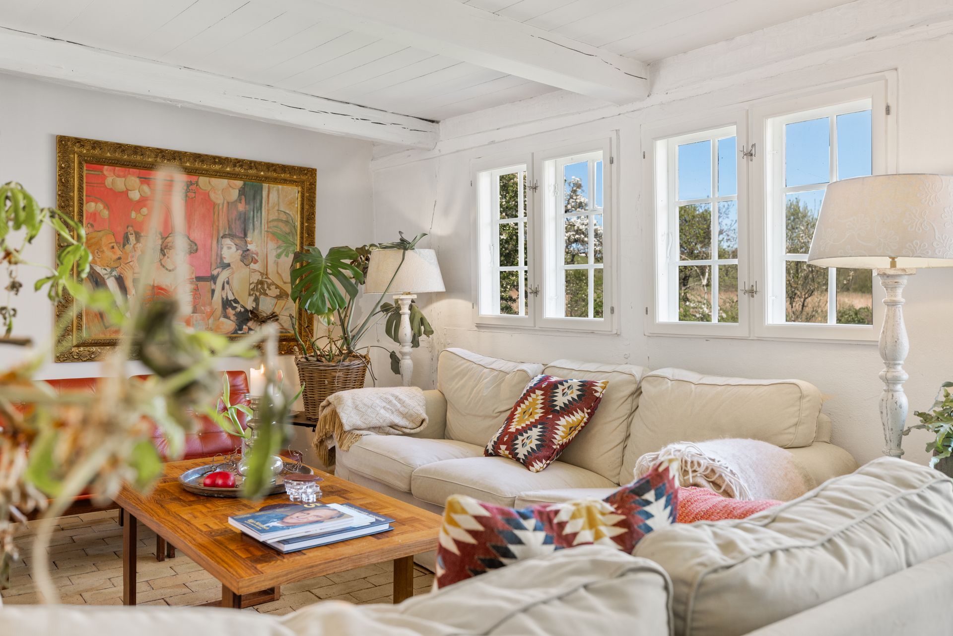 A living room with a couch , table , lamps and a painting on the wall.