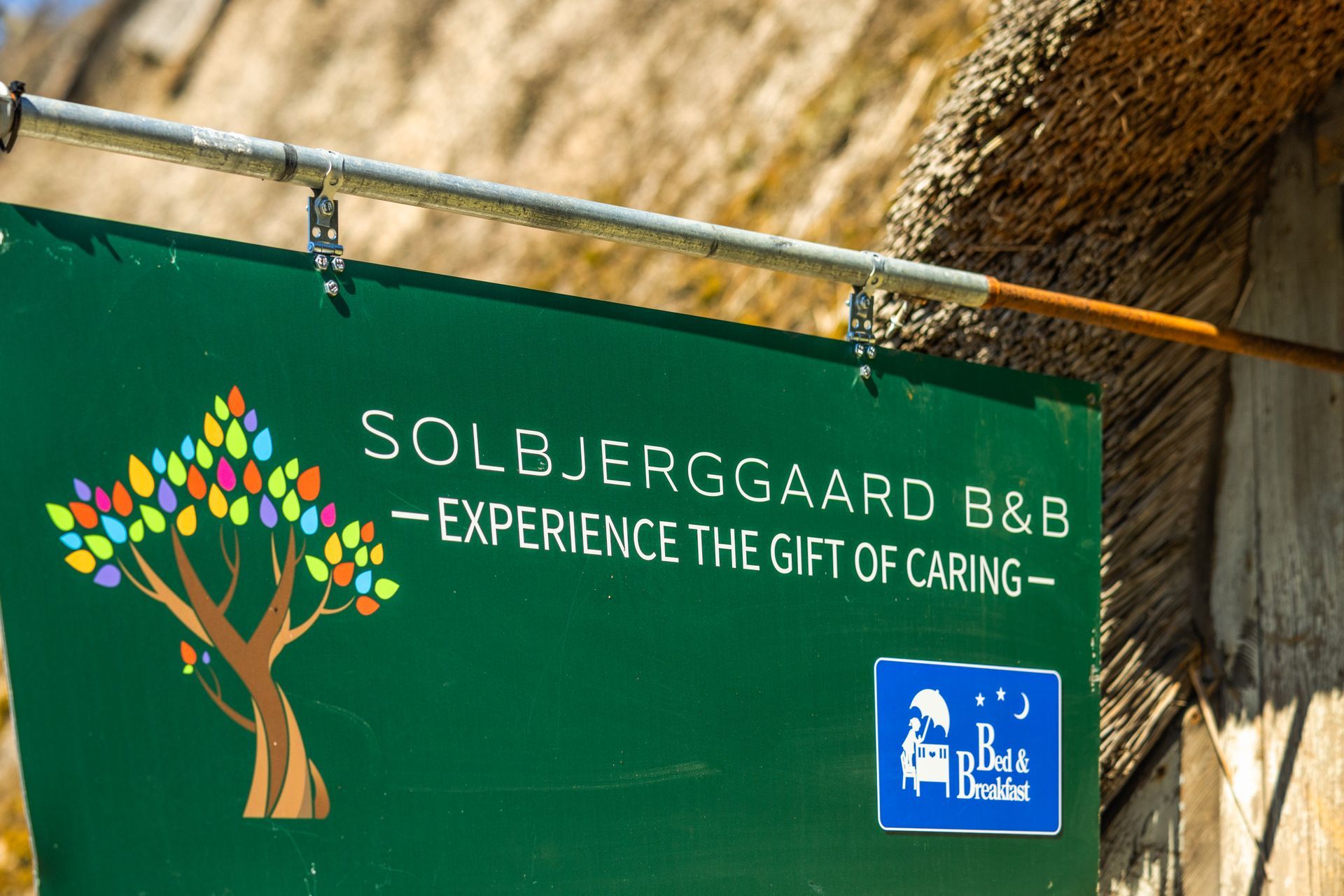 A green sign that says solbjerggaard b & b experience the gift of caring