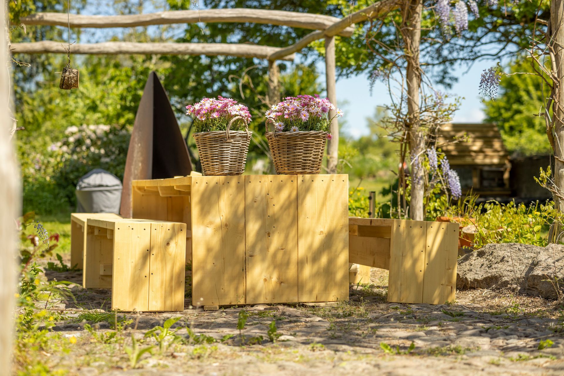 A wooden table with flowers in baskets on it in a garden.