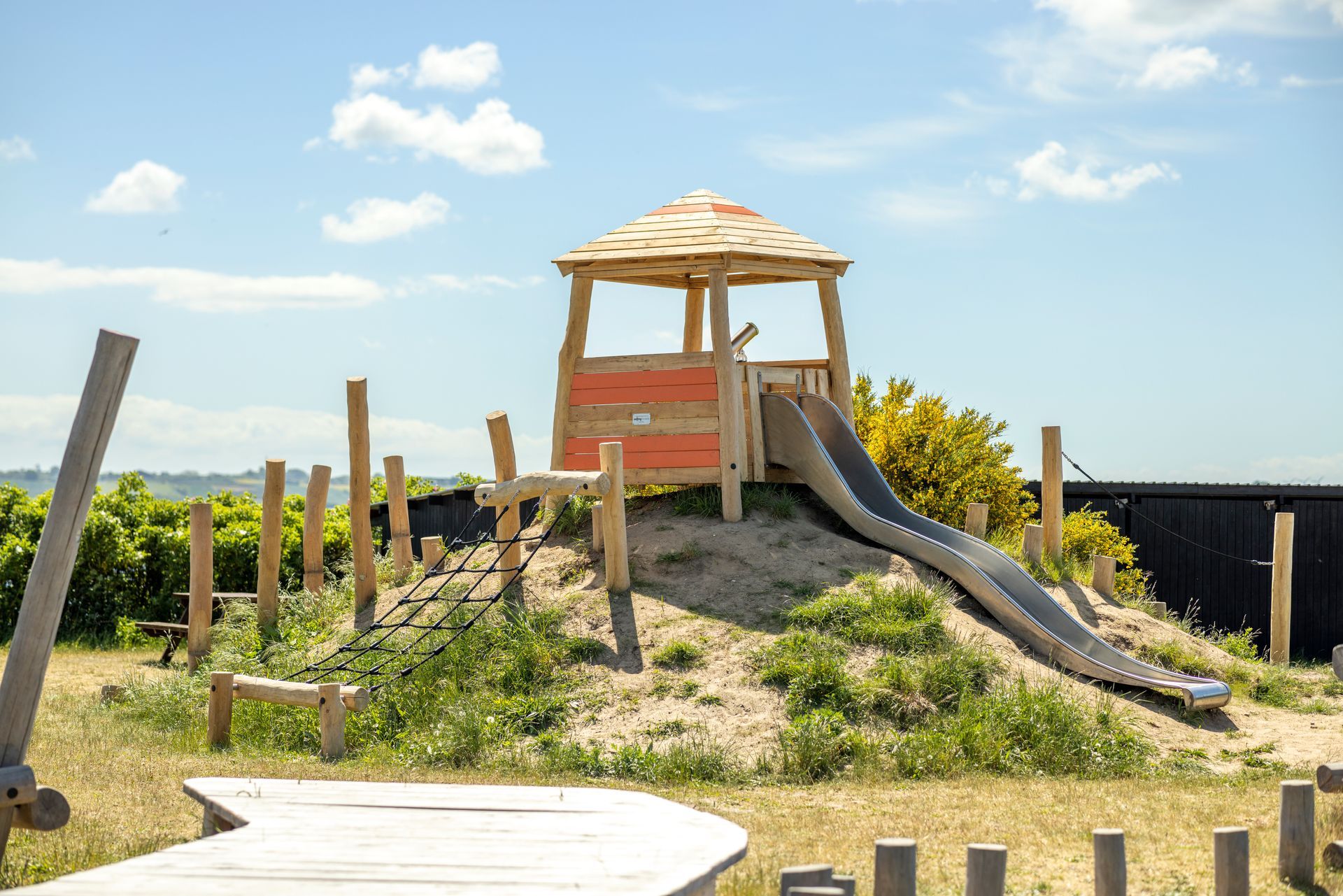A wooden playground with a slide and a tower on top of a hill.