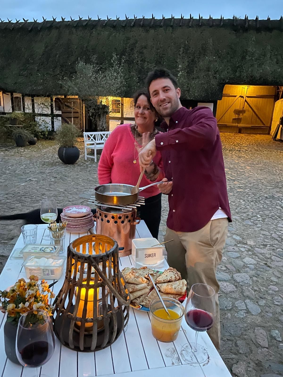 A man and a woman are standing at a table with food and wine.