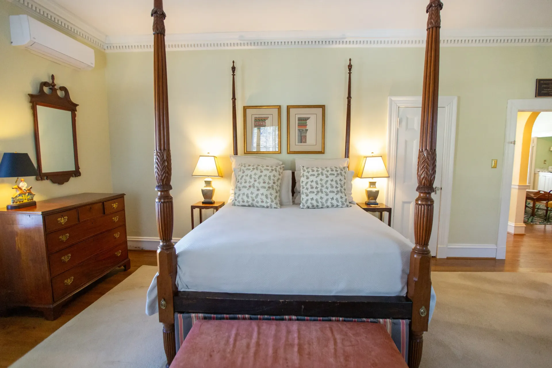 Bedroom with four-poster bed, wood furniture, lamps, beige rug, and doorway leading to another room.