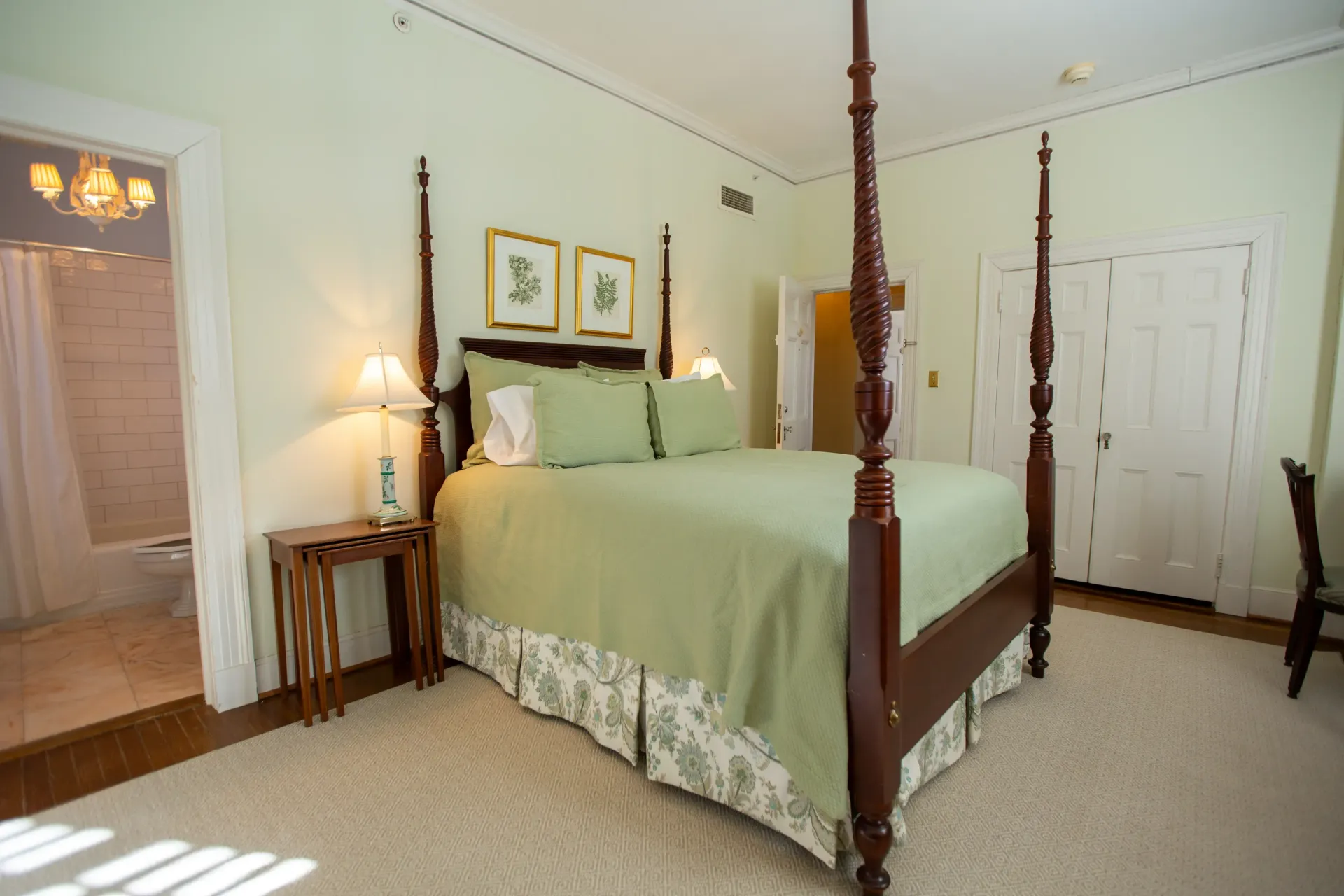Bedroom with a four-poster bed, green bedding, small side table, and open doorway to a bathroom.