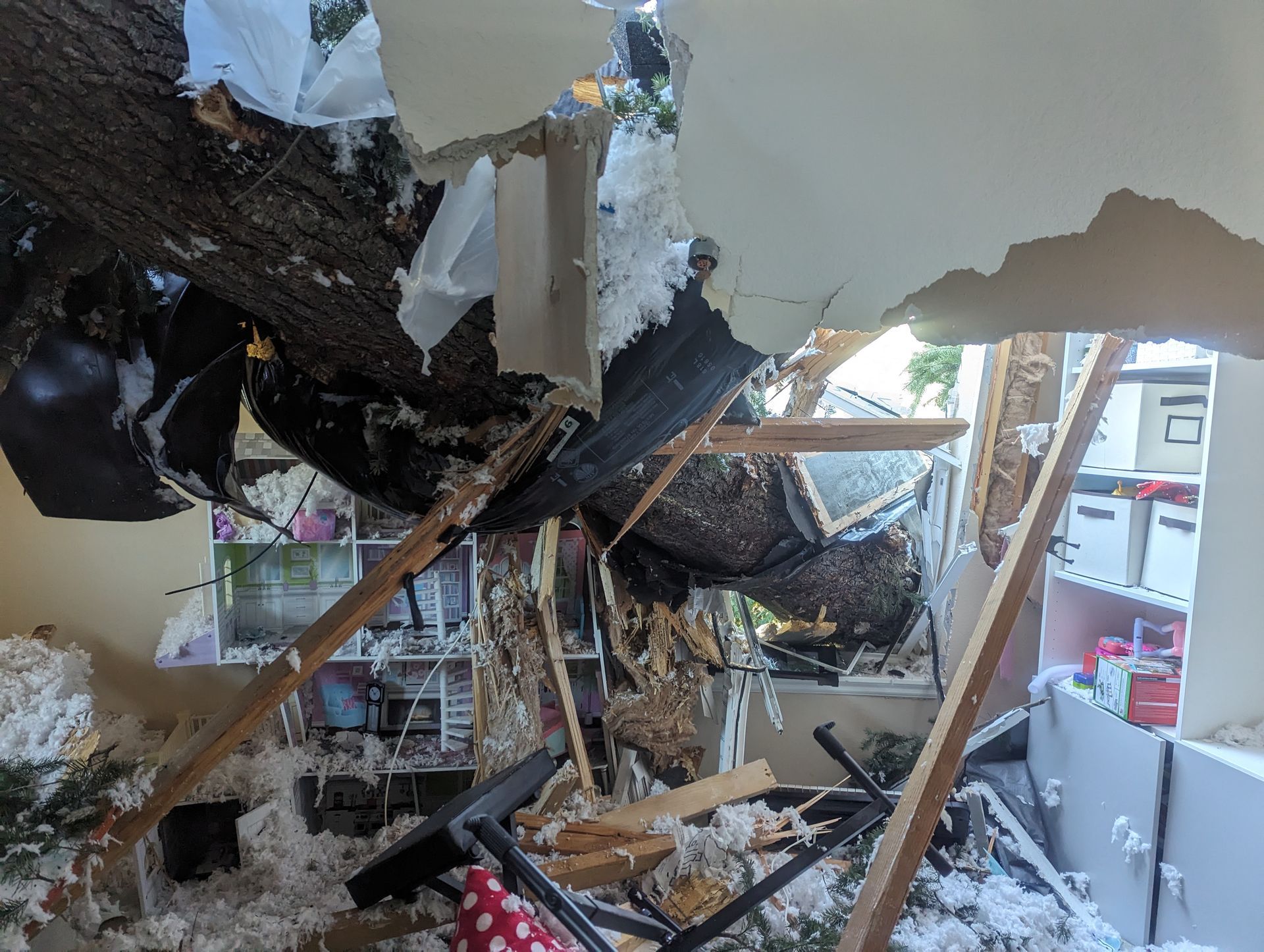 Collapsed ceiling and debris inside a damaged room with a broken wall and exposed beams.
