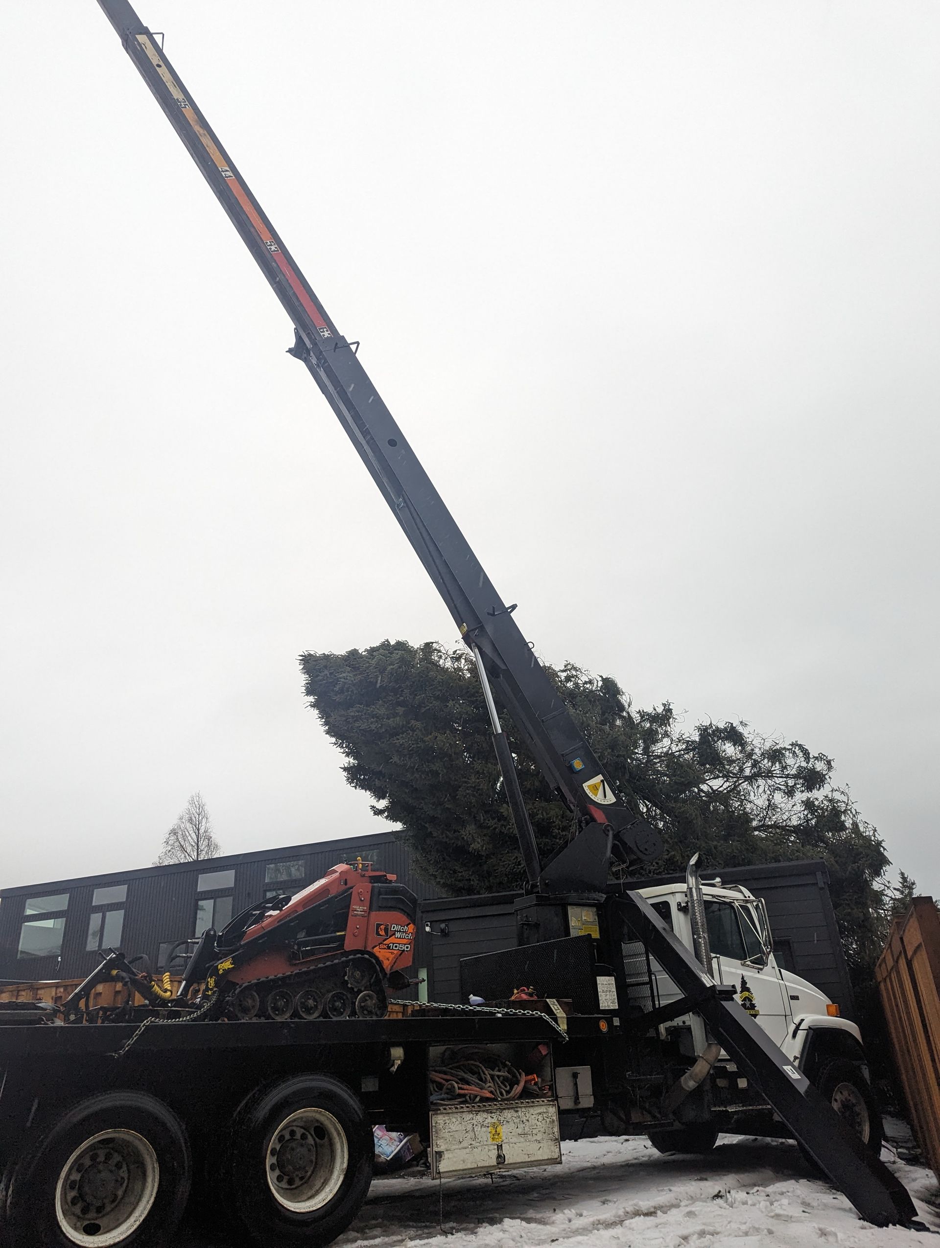 Tow truck lifting a black car with a long crane arm on a street