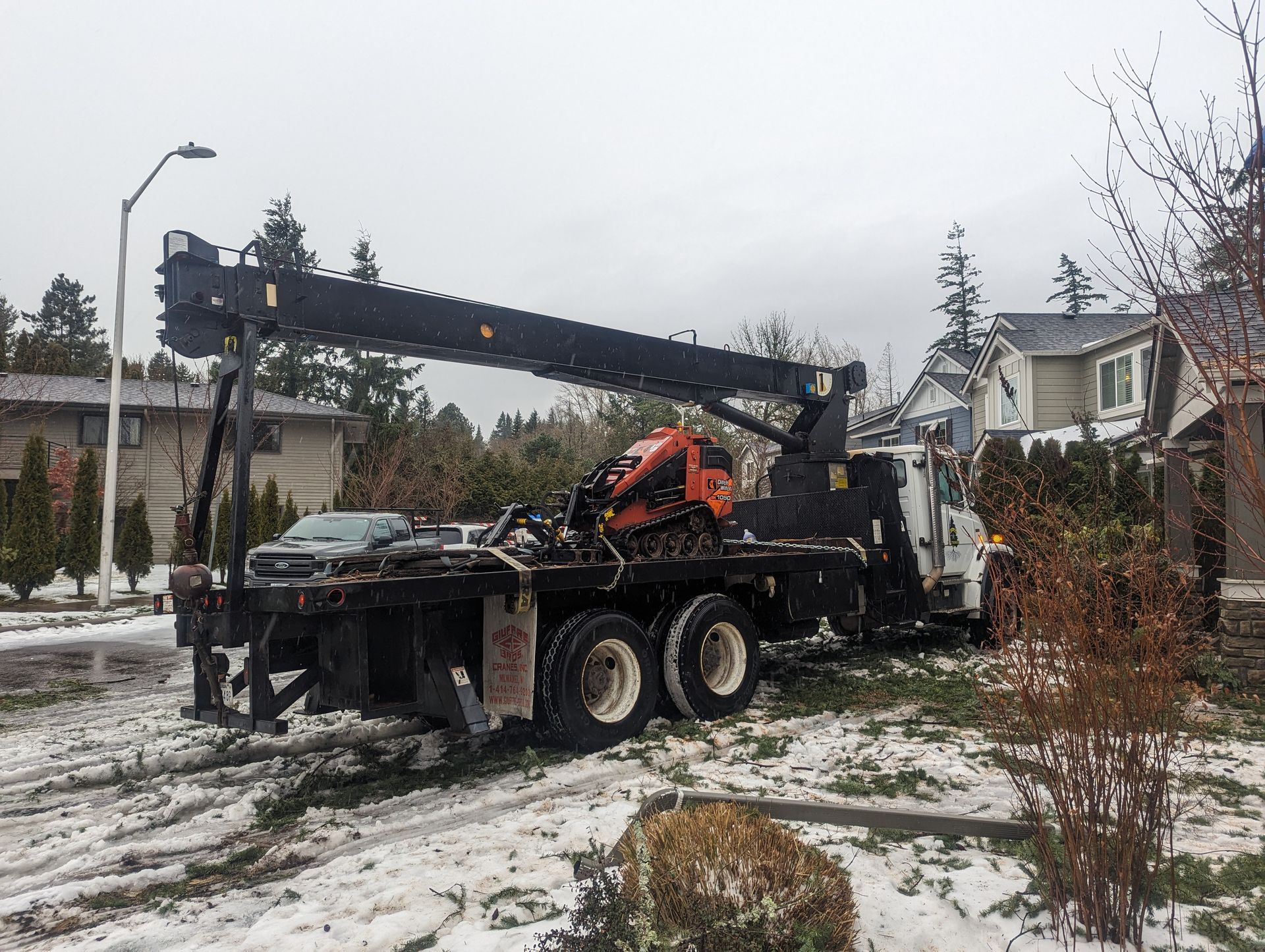 Tow truck with raised boom parked on a snowy residential street after an accident