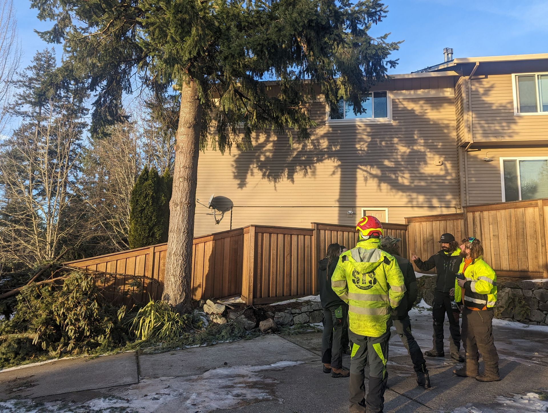 Three workers in high-visibility gear stand beside a suburban house and fence in bright sunlight