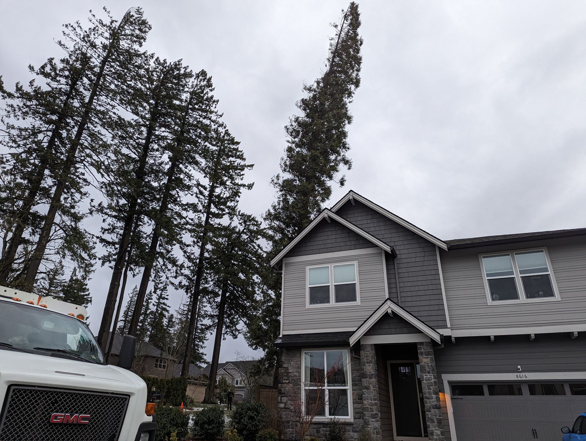 Gray two-story house with a truck parked beside it under a cloudy sky.