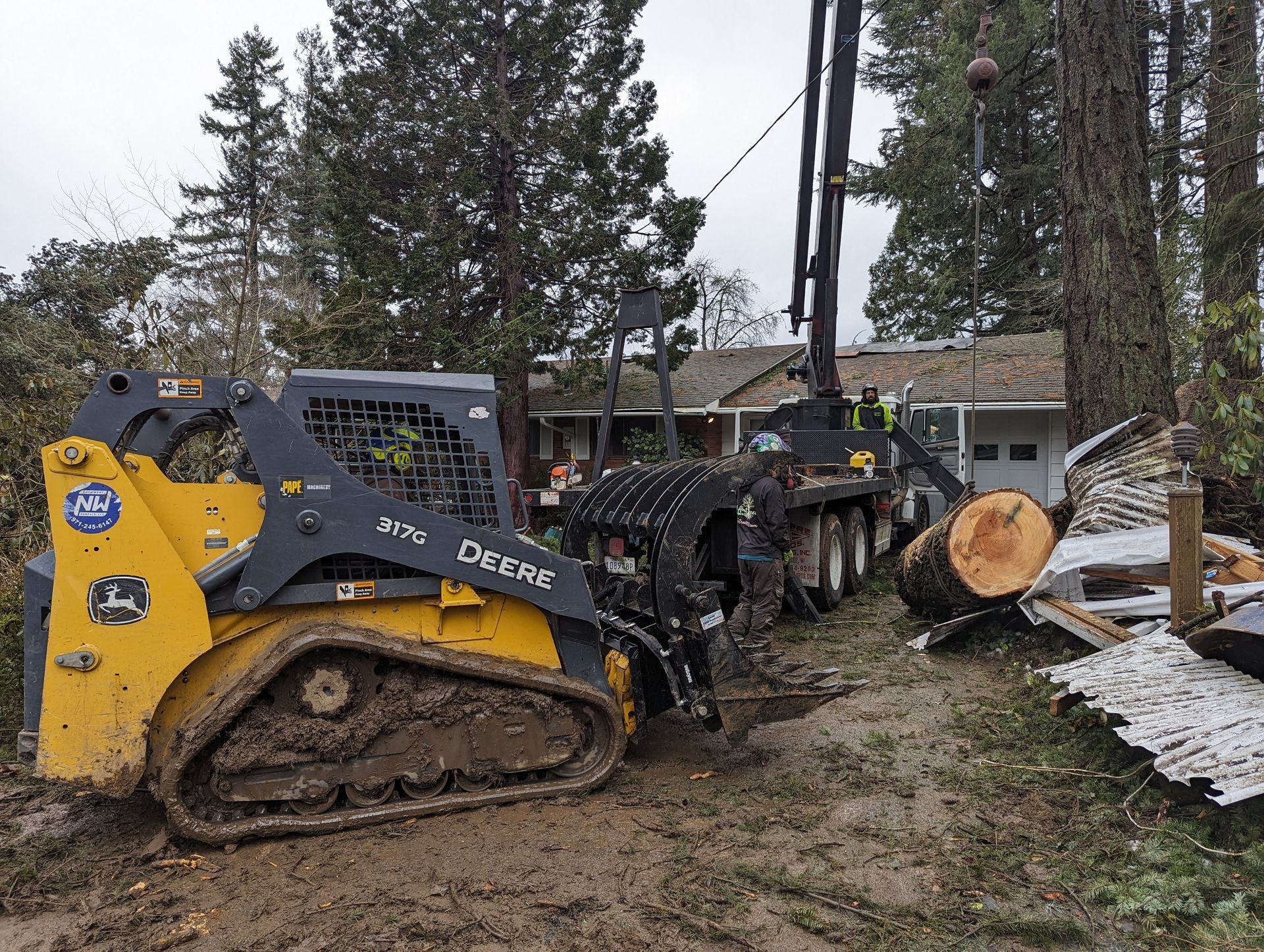Yellow tracked skid steer clearing debris beside a downed tree and log in a muddy yard
