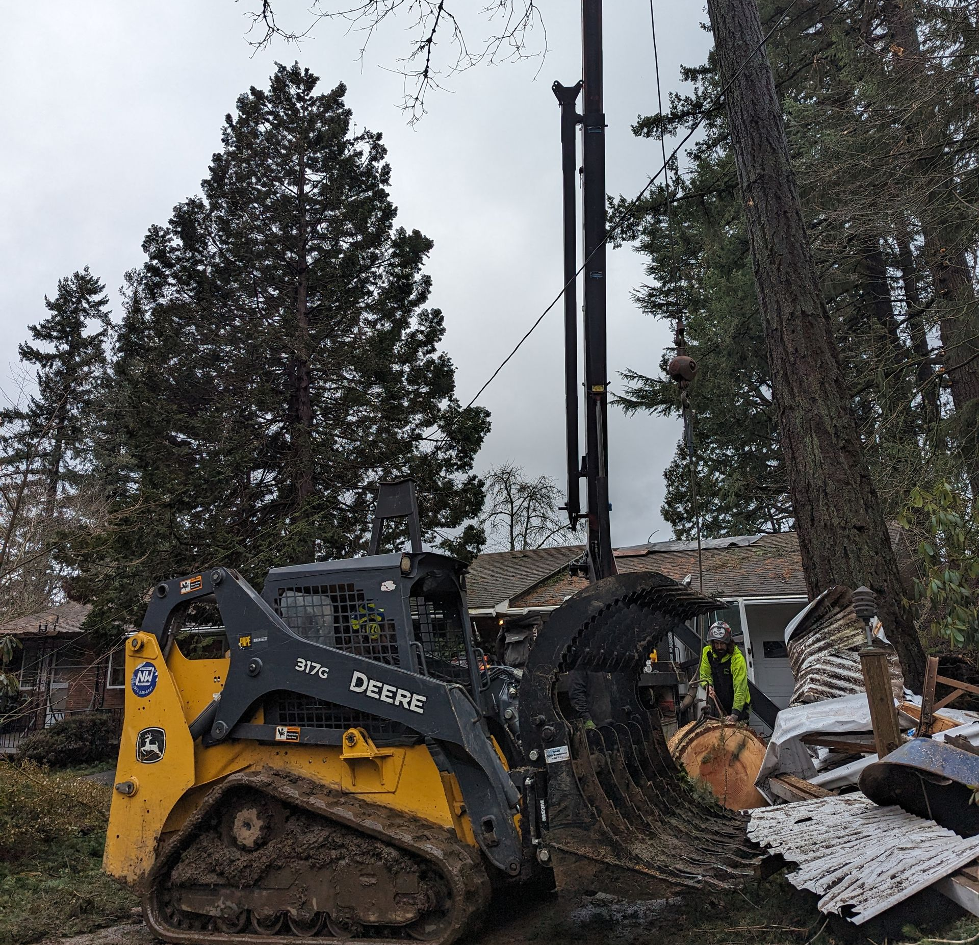 Yellow John Deere excavator clearing debris beside a fallen utility pole in a wooded area.