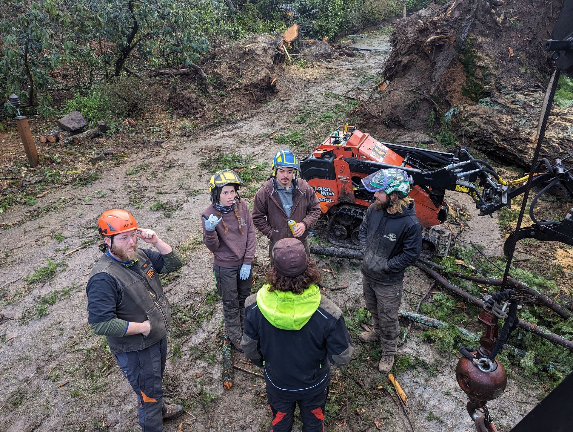 People standing beside an orange ATV in a muddy forest clearing, looking up at the camera.
