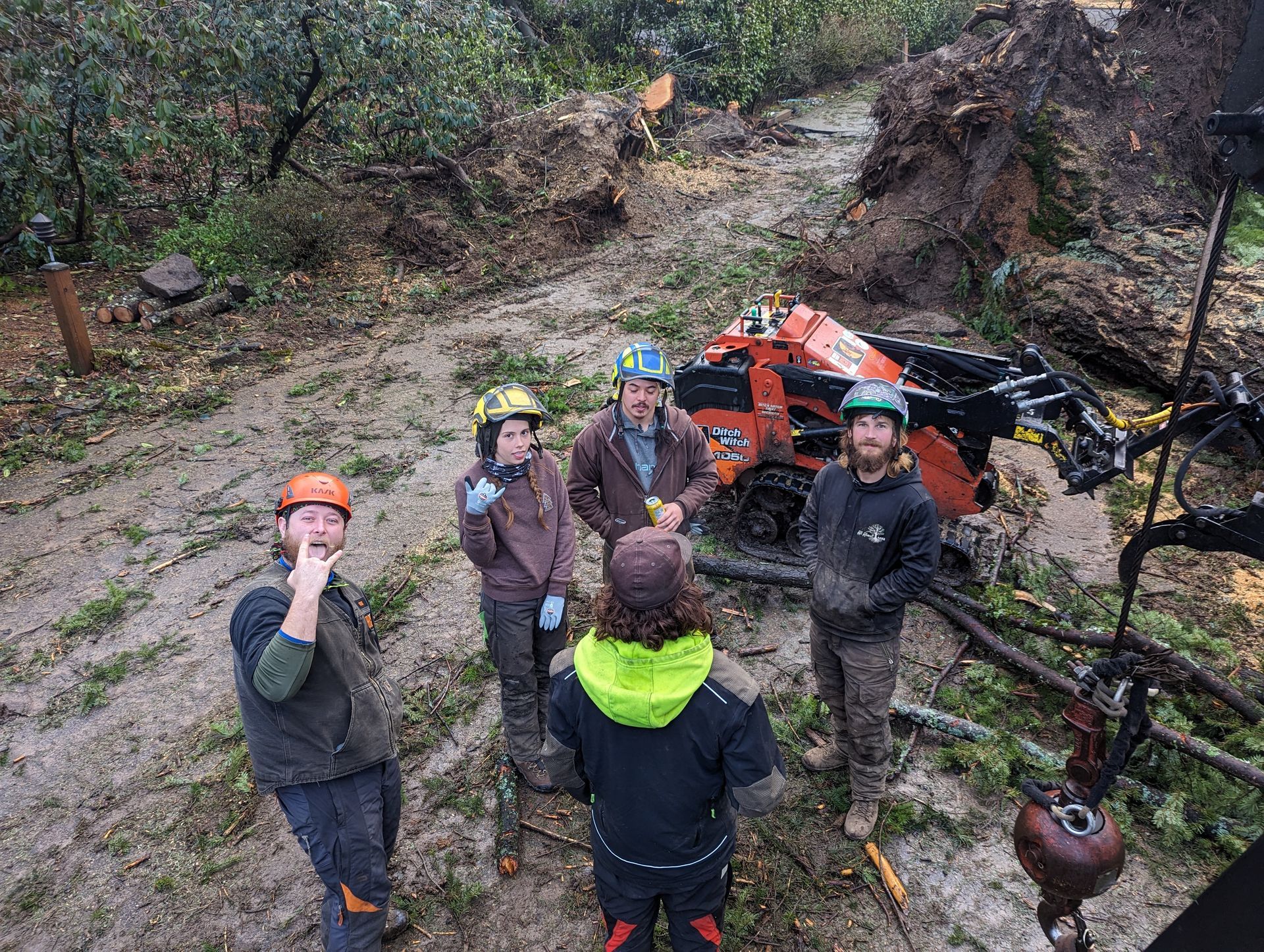 Five helmeted hikers pause on a muddy trail beside an off-road vehicle in a wooded area.