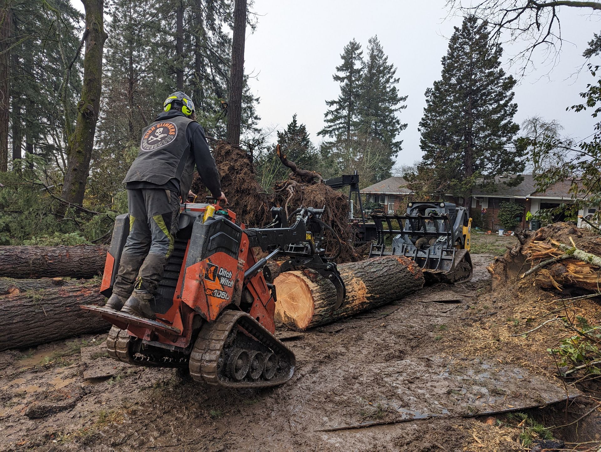 Person operating an orange forestry machine dragging logs through a muddy, wooded area