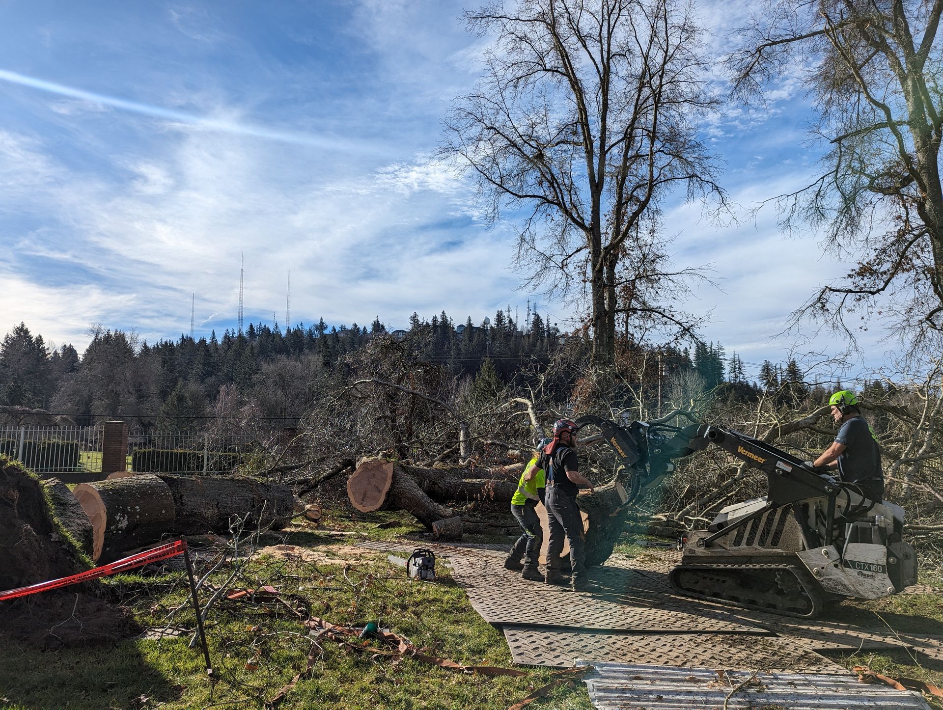 Workers clearing storm debris with a chainsaw in a damaged yard under a blue sky