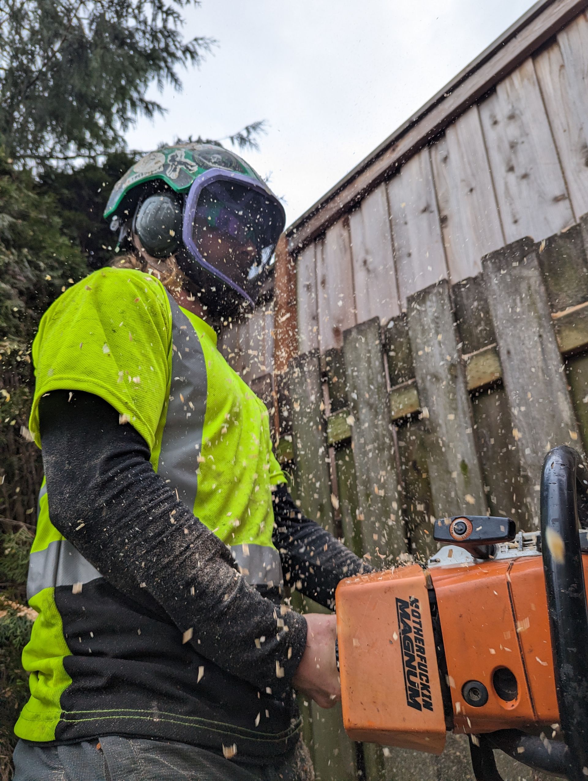 Person in neon yellow safety gear operating a chainsaw outdoors in rainy conditions