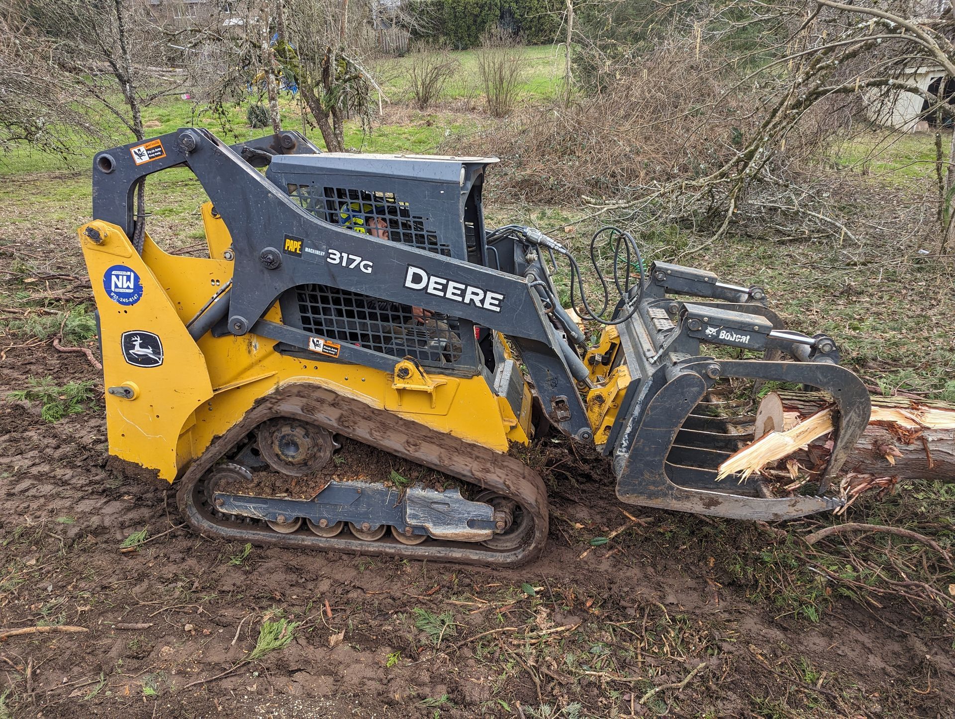 Yellow John Deere skid steer with grapple bucket working on muddy ground outdoors