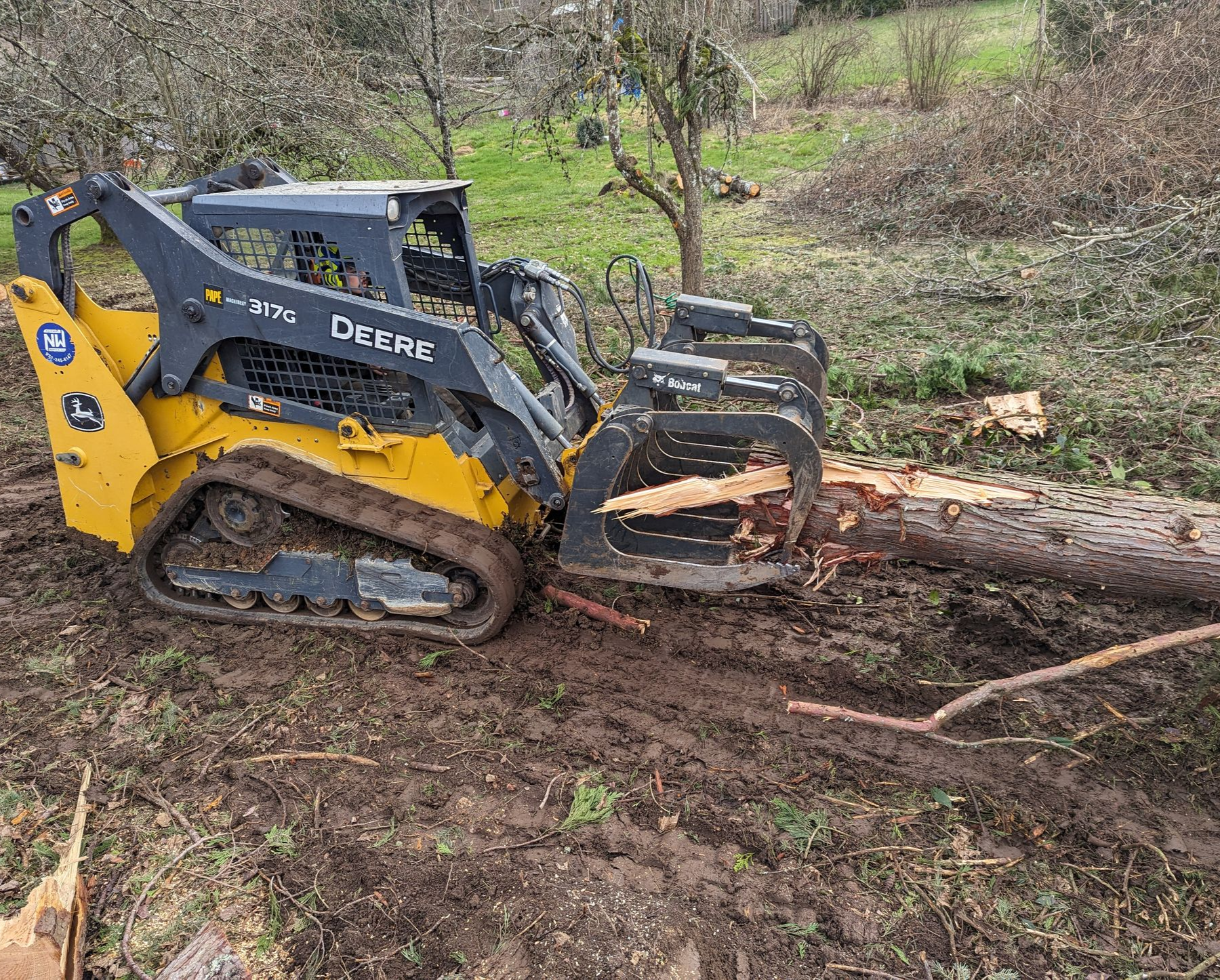 Yellow tracked skid steer pushing a felled log through a muddy wooded area