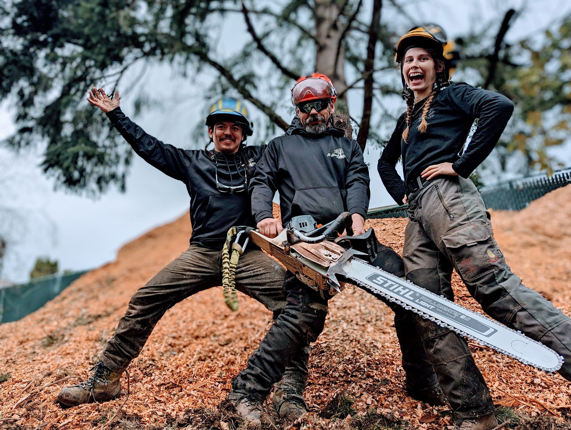 Three muddy mountain bikers posing with a bike on a dirt trail, smiling and cheering.