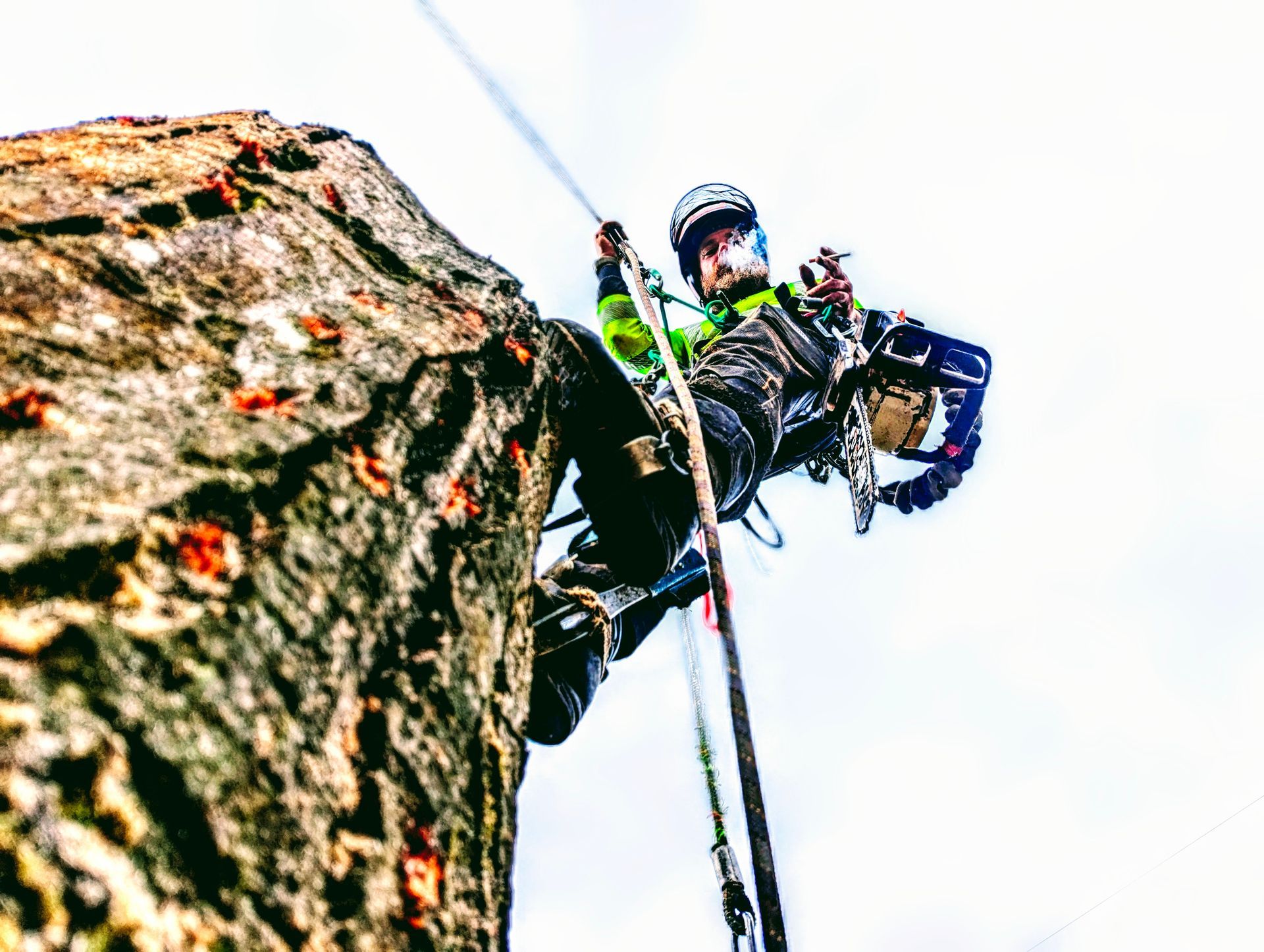 Climber hanging beside a rocky cliff, wearing a helmet and gear, with a rope against a bright sky
