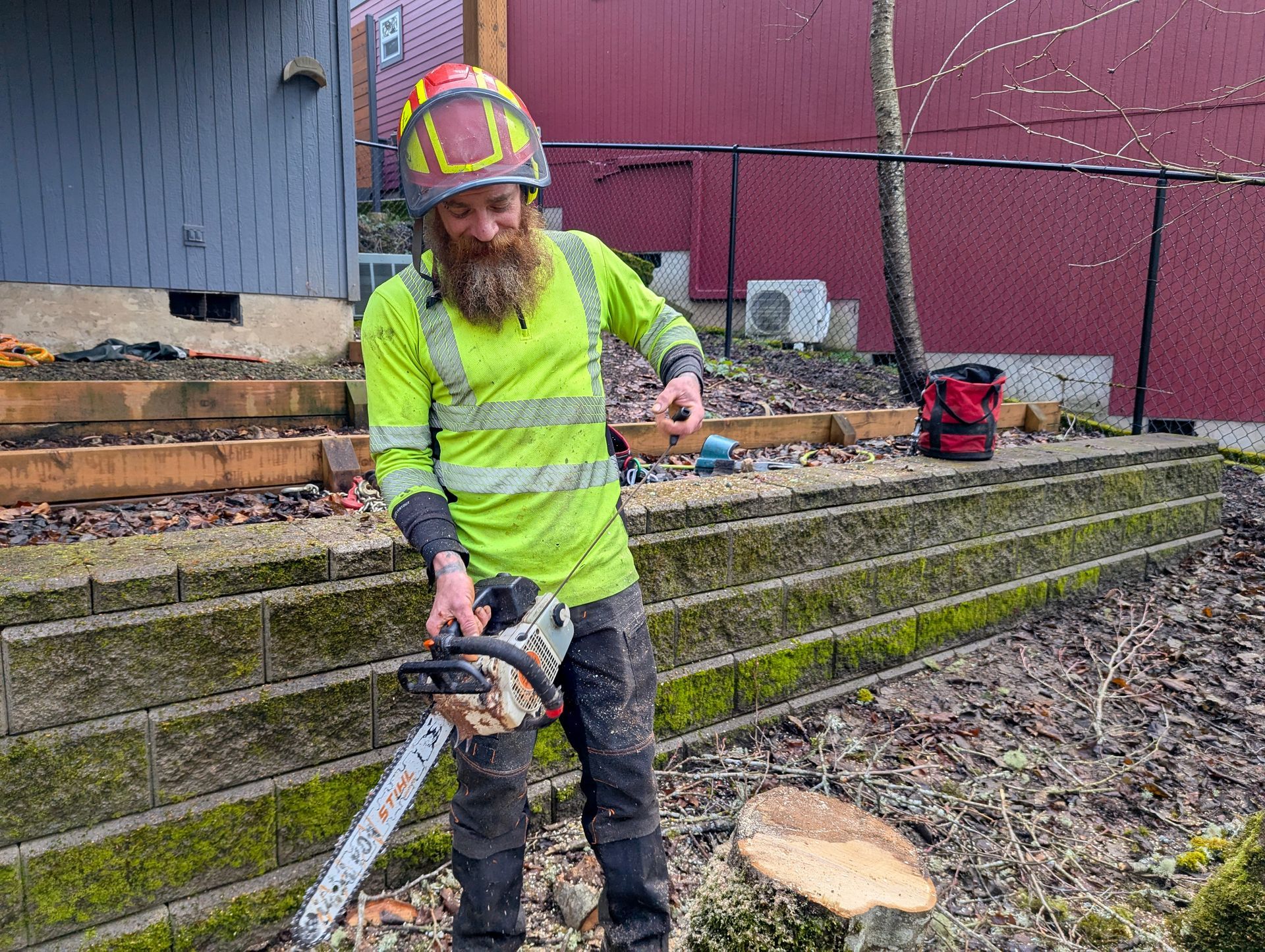 Worker in neon safety gear using a chainsaw beside stacked lumber at a construction site