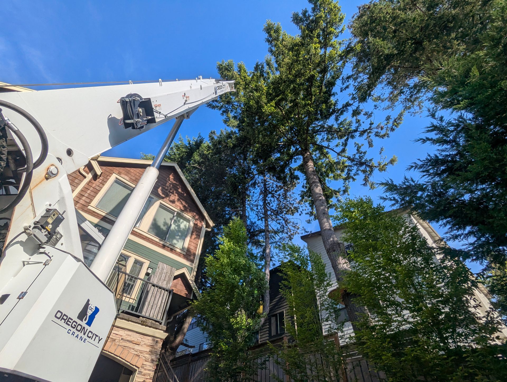 Urban street view with white truck lift, brick house, and tall green trees under a clear blue sky