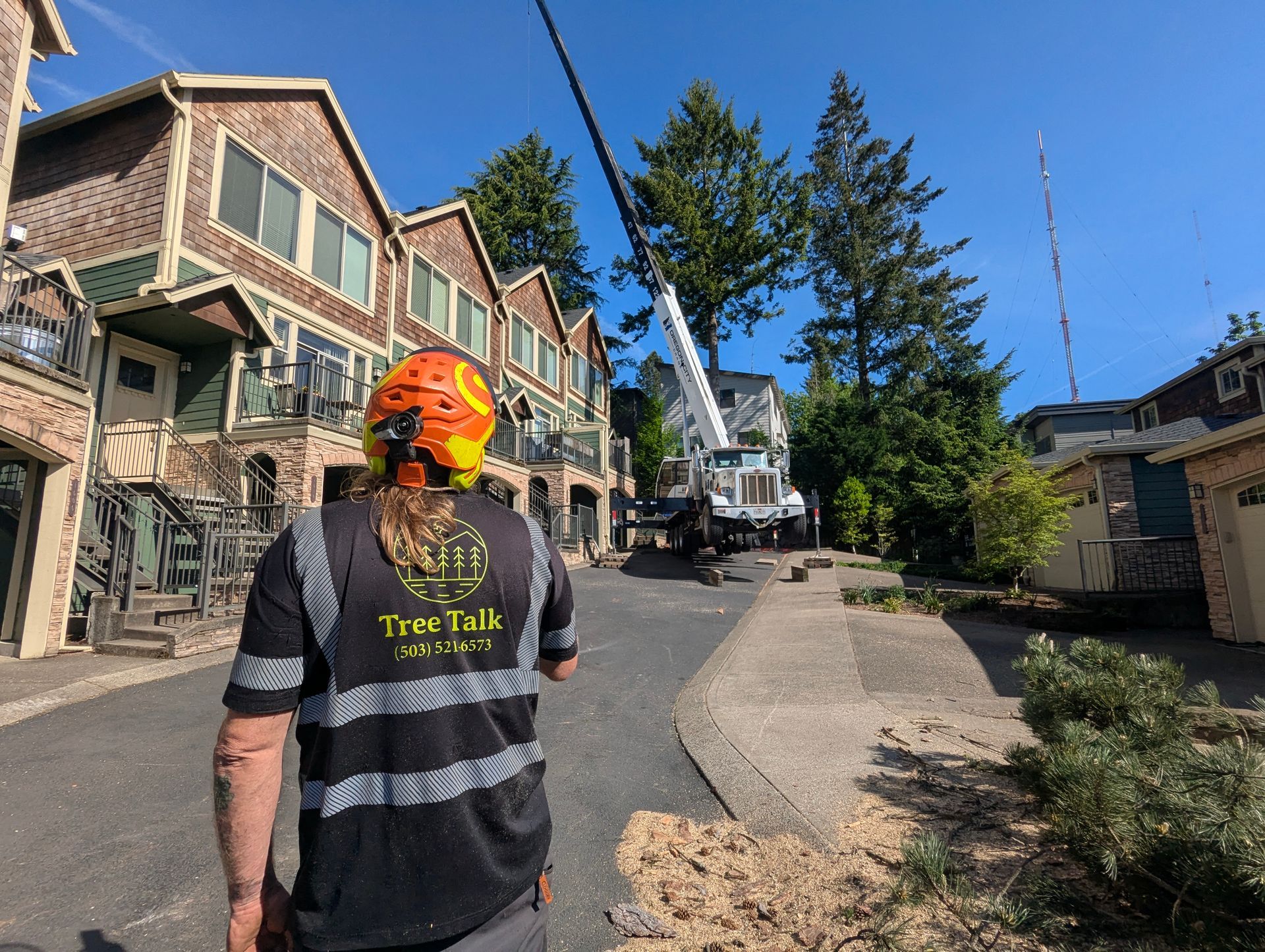 Worker in orange helmet walking on a steep gravel road beside houses and a utility truck