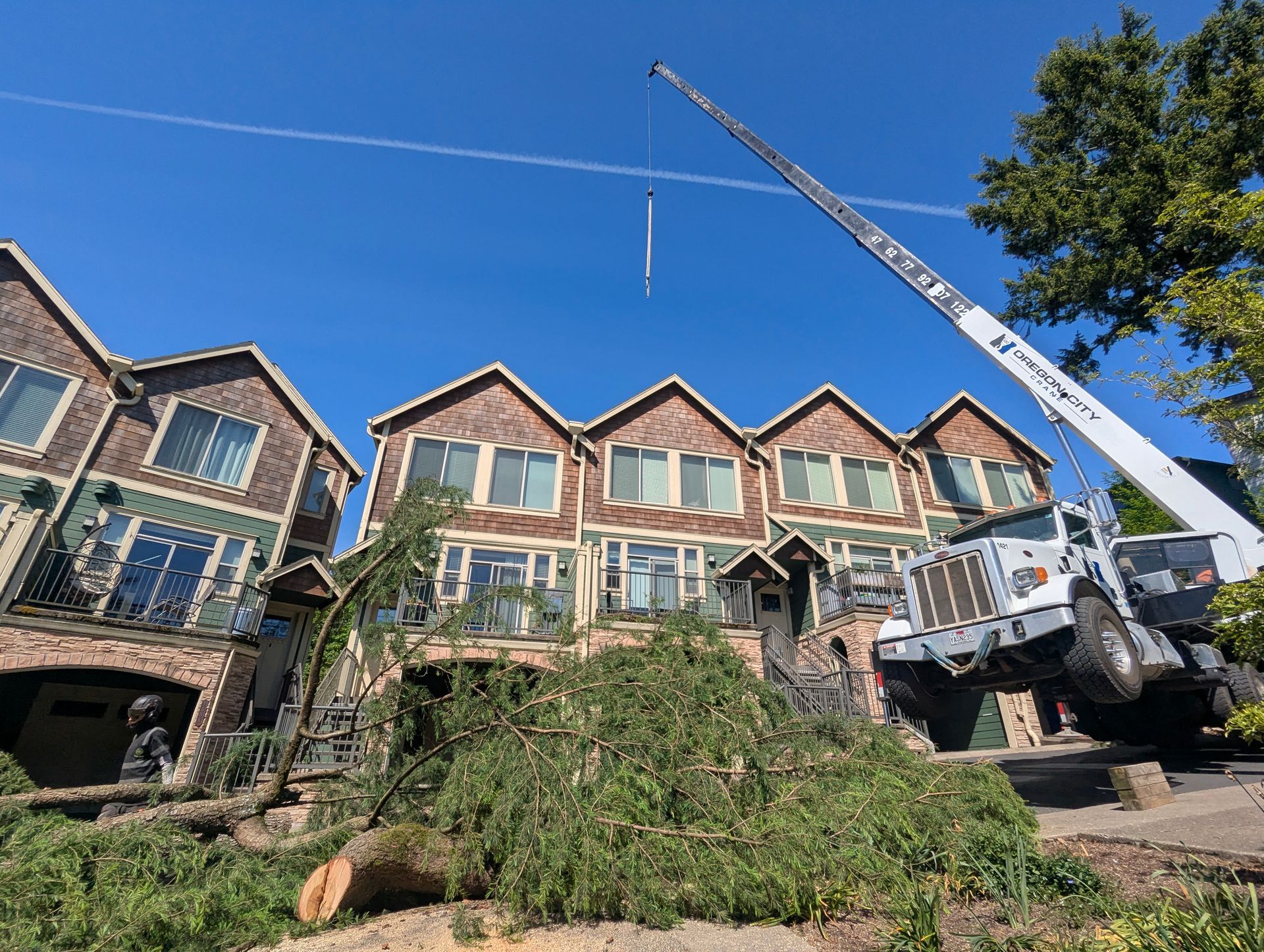 Row of townhouses under construction with a crane and fallen tree debris in front