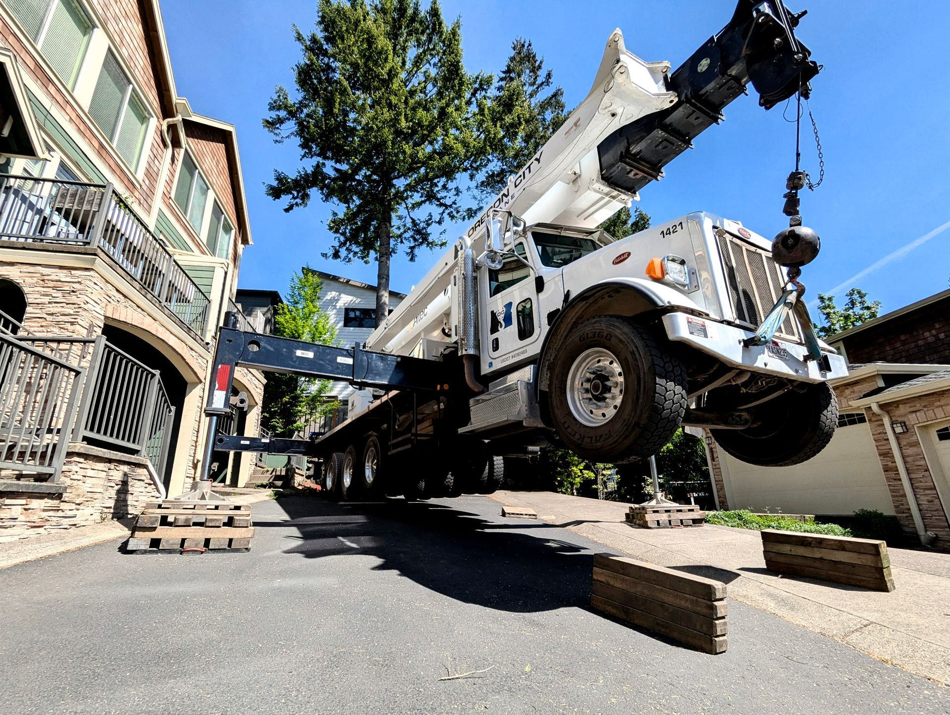 A tow truck lifting a white vehicle on a sloped street beside a damaged building.