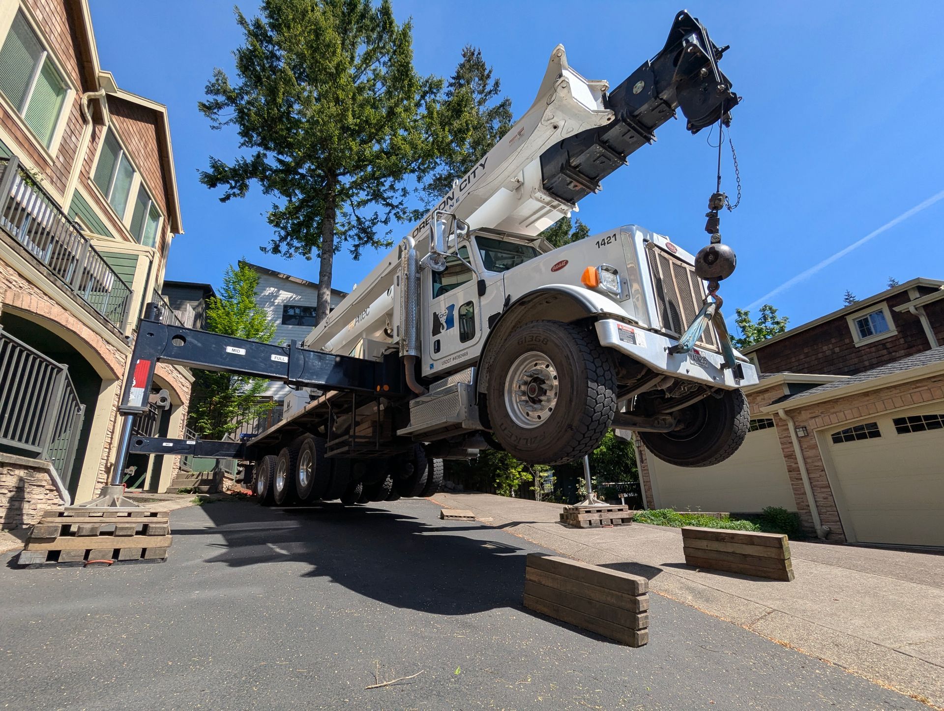 Tow truck lifting a car wheel-first in a driveway beside a brick house and tree