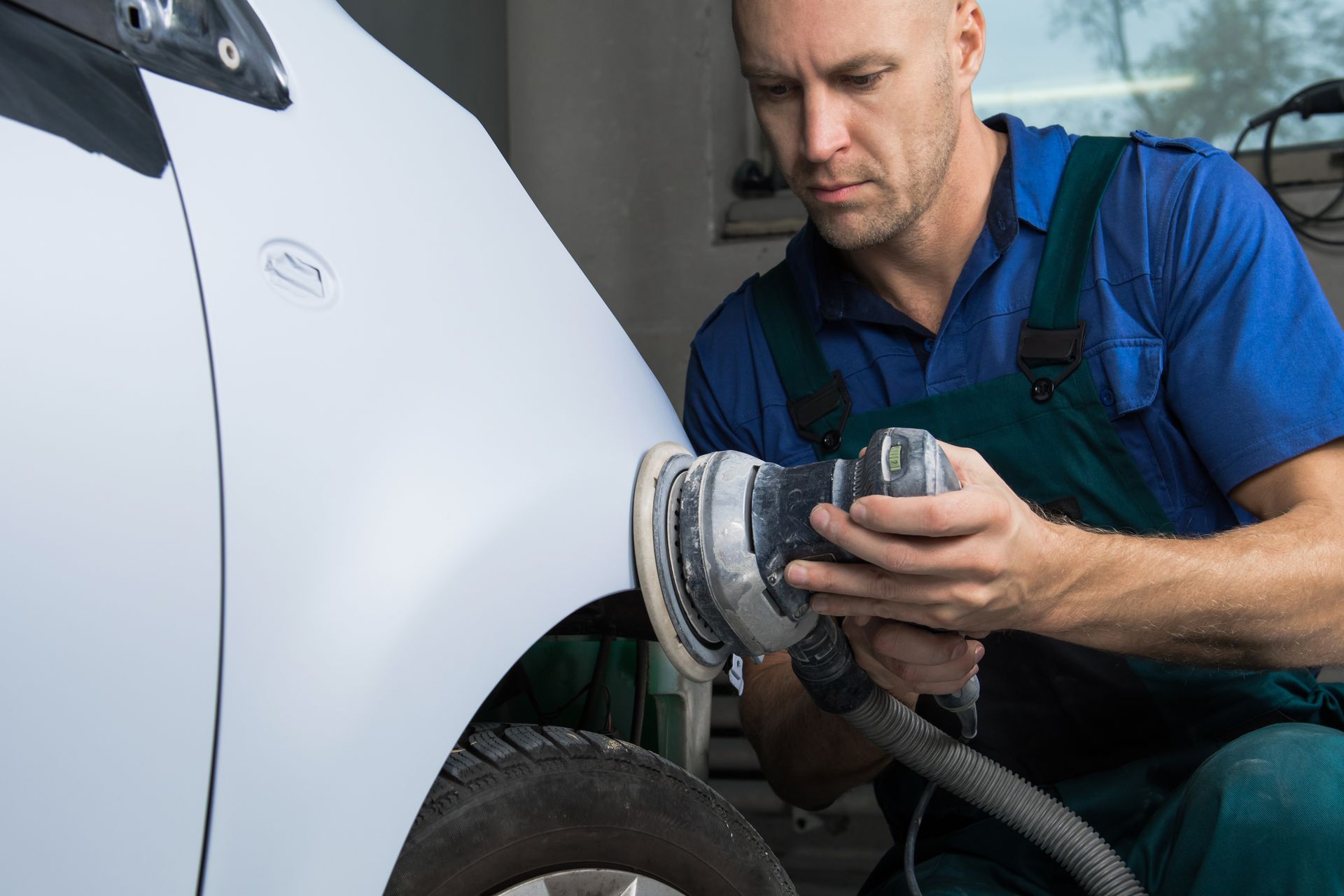 Mechanic polishing a white car panel with an electric buffer in a garage