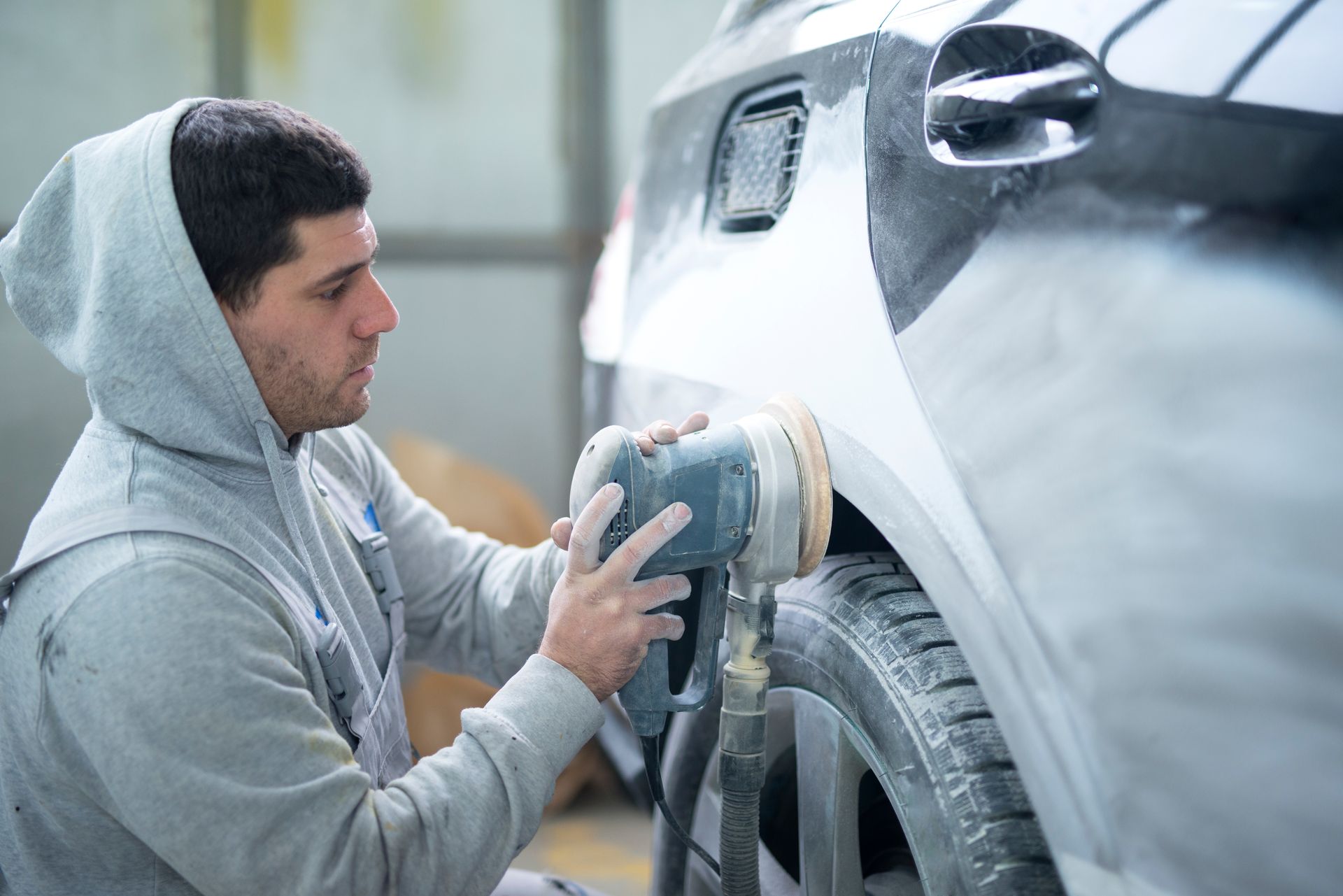 A technician using a power sander on a car body at a professional collision repair shop.