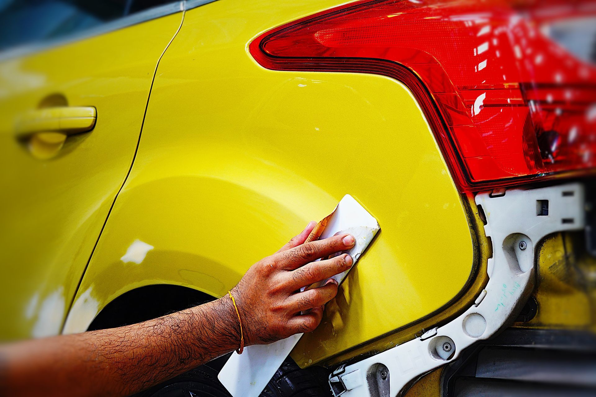 Hand polishing yellow car body near red taillight and rear wheel in auto shop