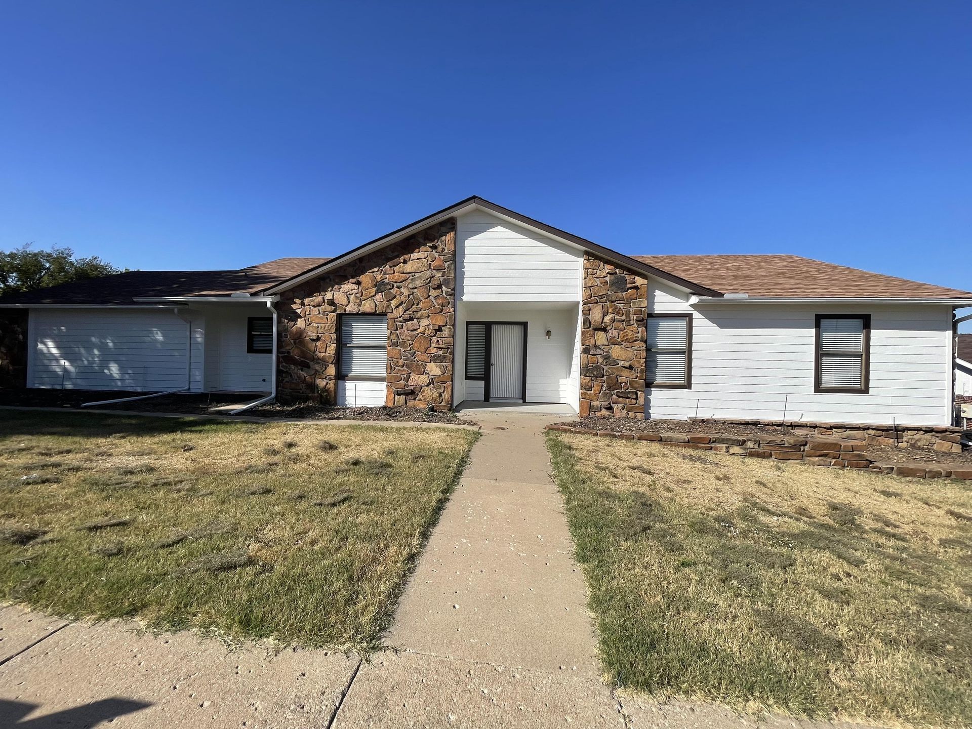 A single-story ranch-style home with a central stone facade, white siding, and a concrete path leading to the front door.