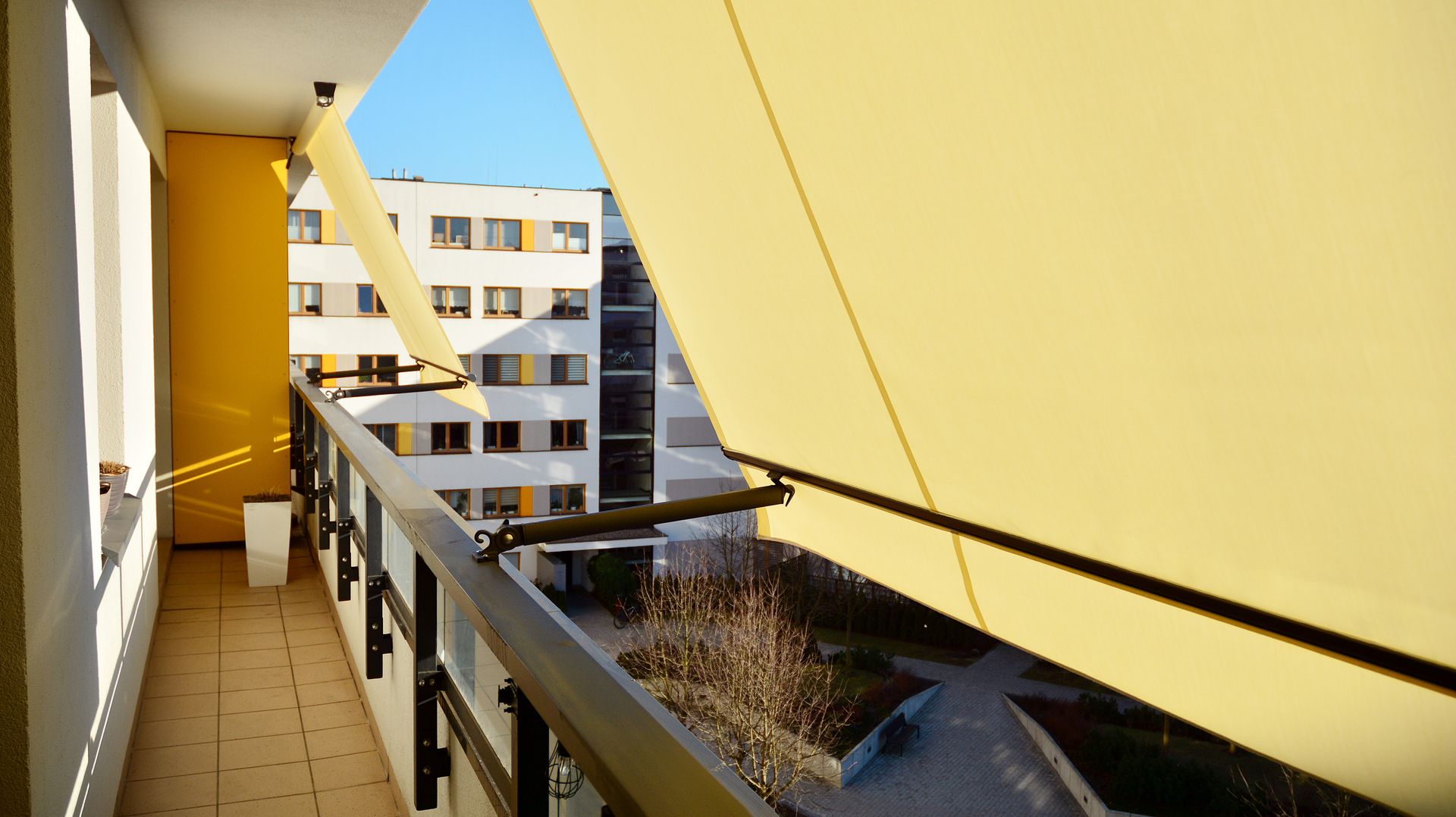 Balcone dell'appartamento con tenda da sole gialla, ringhiera e vista sull'edificio adiacente.