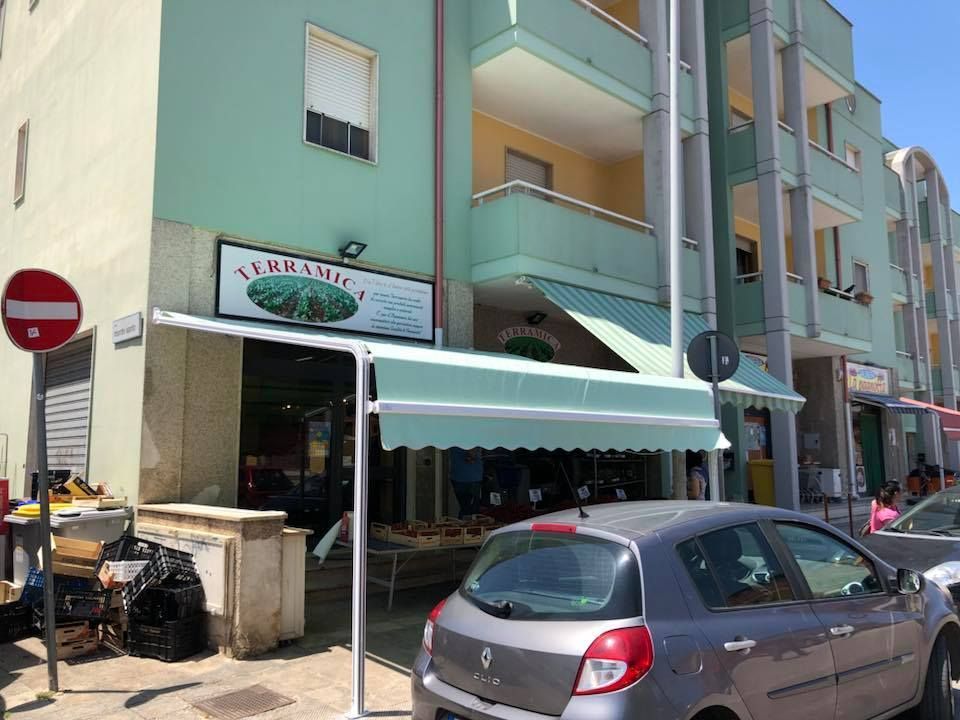Caffè all'aperto con tendalino verde menta e auto parcheggiate accanto a palazzi color pastello.